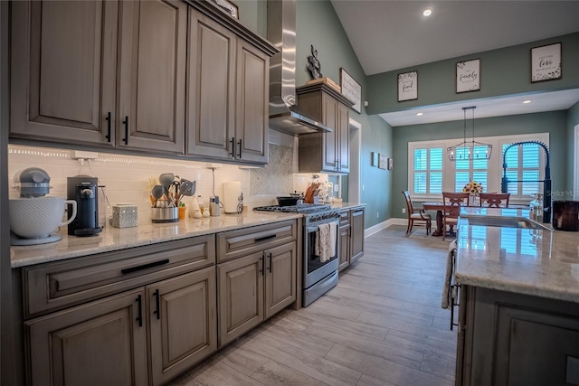 kitchen featuring light wood-type flooring, decorative backsplash, stainless steel gas stove, and wall chimney exhaust hood