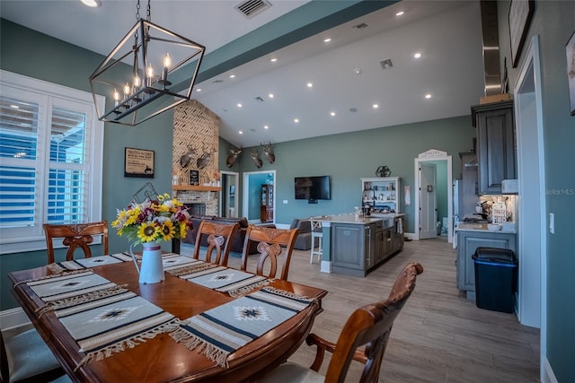 dining room featuring a fireplace, high vaulted ceiling, a chandelier, and light wood-type flooring