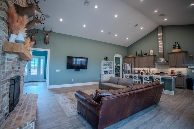 living room with a brick fireplace, sink, high vaulted ceiling, and light hardwood / wood-style flooring