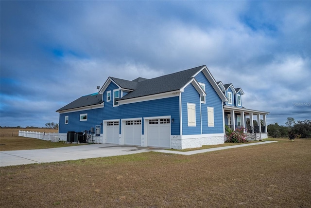 view of side of property with a lawn, central AC unit, a garage, and covered porch