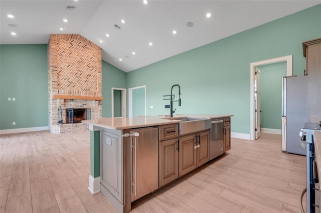 2437 Bay Lake Loop, Groveland, FL 34736 - kitchen featuring appliances with stainless steel finishes, a center island with sink, light wood-style floors, light countertops, and a fireplace