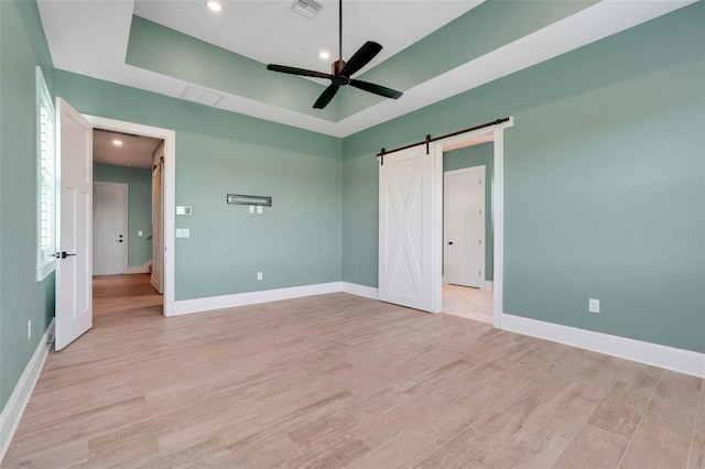 2437 Bay Lake Loop, Groveland, FL 34736 - unfurnished bedroom featuring a barn door, light wood-type flooring, a raised ceiling, recessed lighting, and ceiling fan