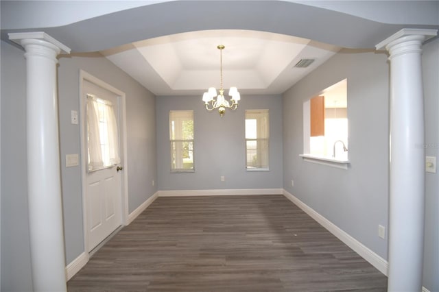 unfurnished dining area featuring sink, dark hardwood / wood-style floors, a notable chandelier, a tray ceiling, and ornate columns