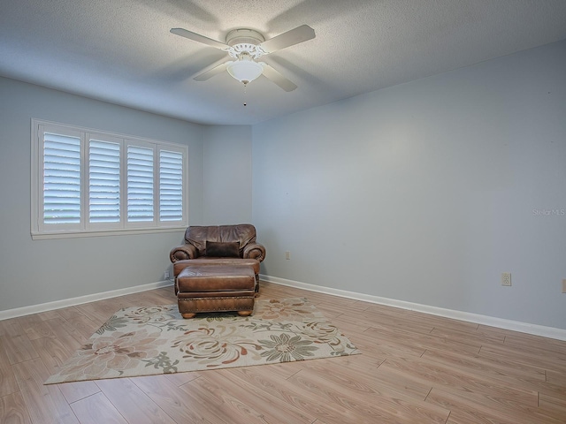 sitting room with ceiling fan, a textured ceiling, and light wood-type flooring