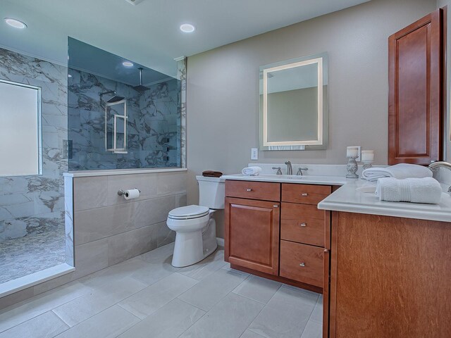 bathroom with vanity, tile patterned flooring, toilet, tiled shower, and tile walls