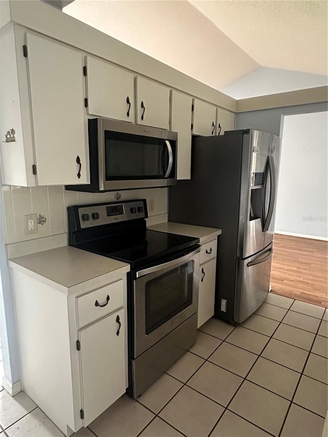 kitchen featuring backsplash, vaulted ceiling, light tile patterned flooring, white cabinetry, and stainless steel appliances