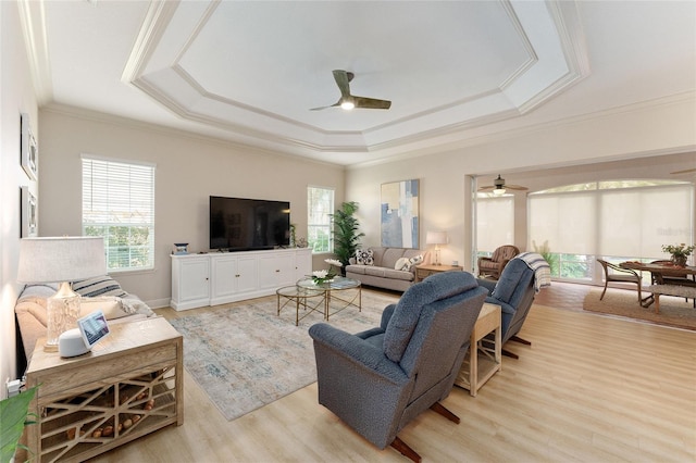 living room with a tray ceiling, ceiling fan, crown molding, and light hardwood / wood-style floors