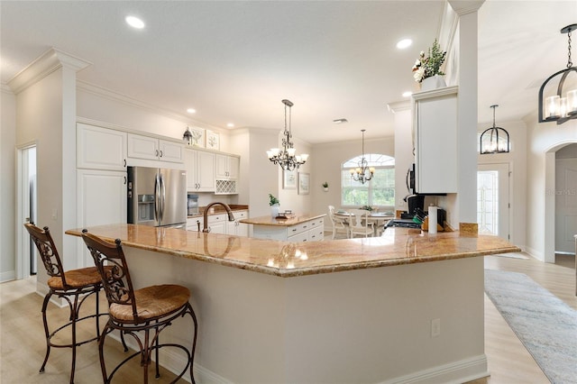 kitchen with kitchen peninsula, stainless steel fridge, light hardwood / wood-style flooring, and hanging light fixtures