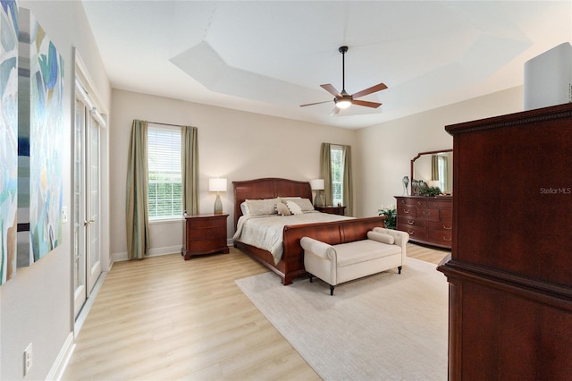 bedroom featuring ceiling fan, light wood-type flooring, and a tray ceiling