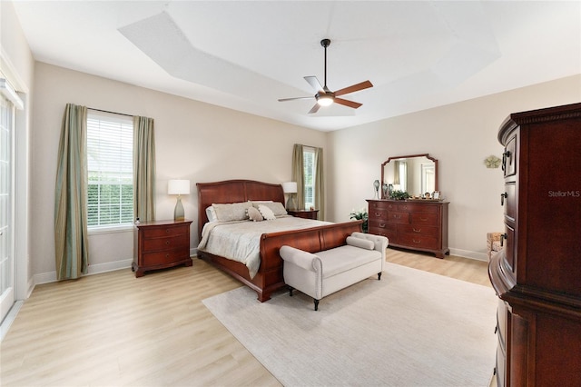 bedroom featuring ceiling fan, light wood-type flooring, and a tray ceiling