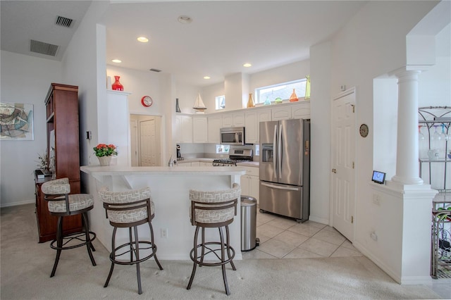 kitchen featuring appliances with stainless steel finishes, white cabinetry, a kitchen breakfast bar, kitchen peninsula, and light tile patterned floors