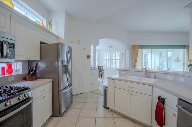 kitchen featuring appliances with stainless steel finishes, white cabinetry, ornate columns, sink, and light tile patterned floors