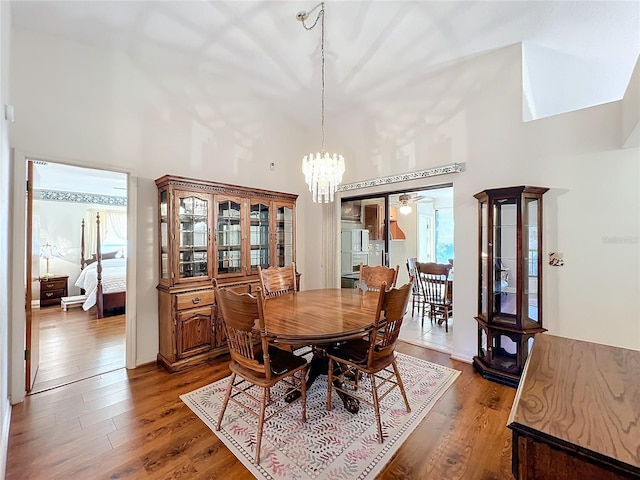 dining space featuring ceiling fan with notable chandelier, a high ceiling, and hardwood / wood-style flooring