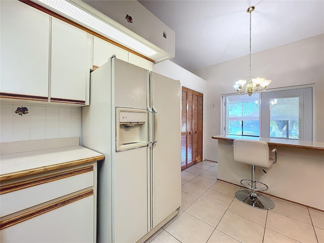 kitchen with hanging light fixtures, decorative backsplash, white fridge with ice dispenser, light tile patterned floors, and white cabinetry