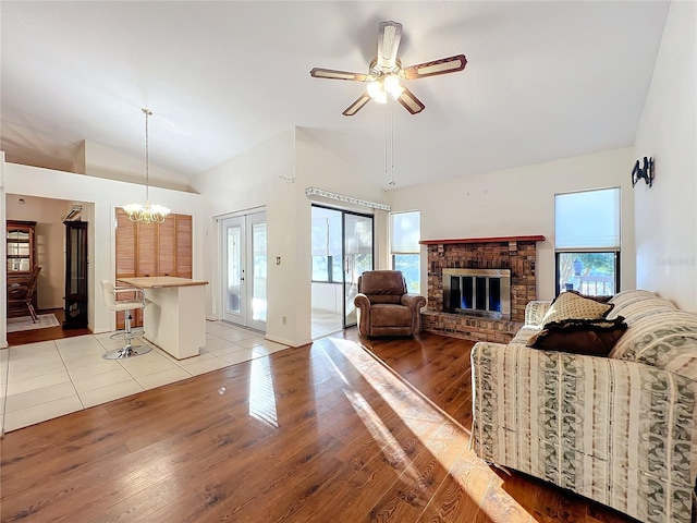 living room with a fireplace, high vaulted ceiling, light hardwood / wood-style floors, and ceiling fan with notable chandelier