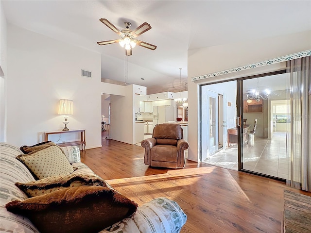 living room featuring lofted ceiling, light wood-type flooring, and ceiling fan with notable chandelier