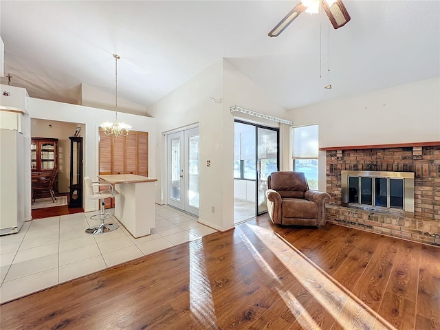 living room featuring ceiling fan with notable chandelier, light wood-type flooring, high vaulted ceiling, and a brick fireplace