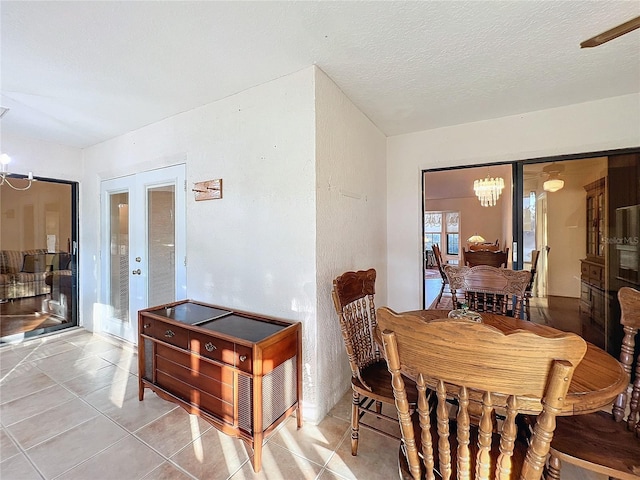 tiled dining space with french doors, a textured ceiling, and a notable chandelier