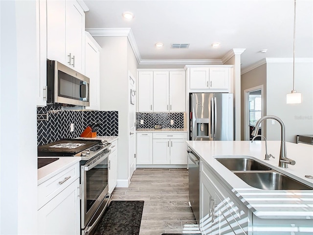 kitchen with stainless steel appliances, sink, light hardwood / wood-style flooring, white cabinets, and hanging light fixtures