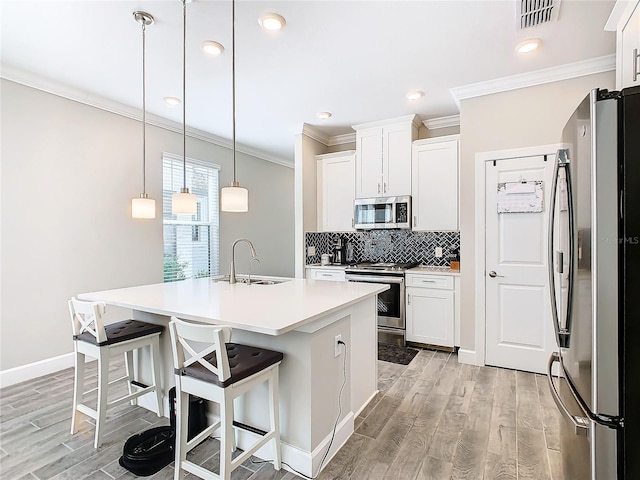 kitchen featuring sink, stainless steel appliances, decorative light fixtures, a kitchen island with sink, and white cabinets