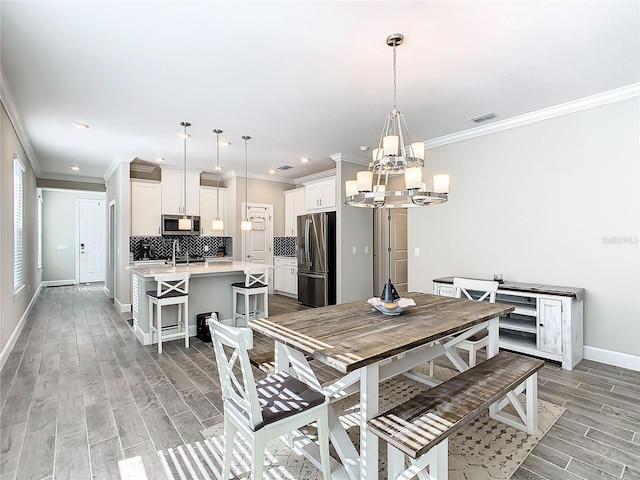 dining area featuring light hardwood / wood-style floors, sink, crown molding, and a chandelier