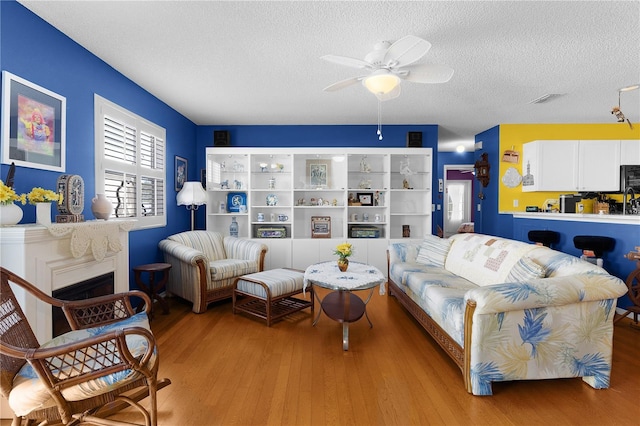 living room with a fireplace, hardwood / wood-style floors, a textured ceiling, and ceiling fan