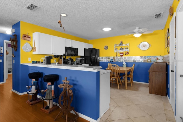 kitchen featuring a kitchen breakfast bar, kitchen peninsula, white cabinetry, and black appliances