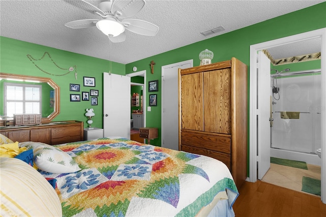 bedroom with a textured ceiling, ensuite bathroom, ceiling fan, and hardwood / wood-style flooring