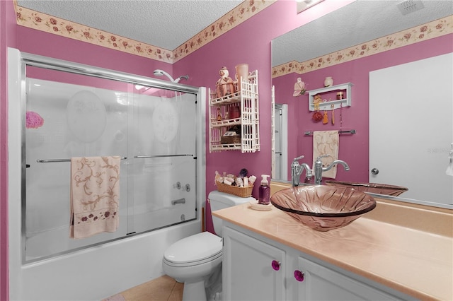 full bathroom featuring vanity, shower / bath combination with glass door, tile patterned floors, toilet, and a textured ceiling