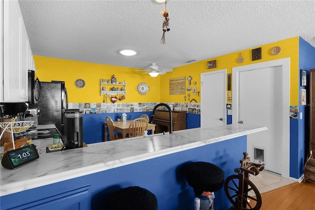 kitchen with white cabinets, light stone counters, a kitchen bar, and kitchen peninsula