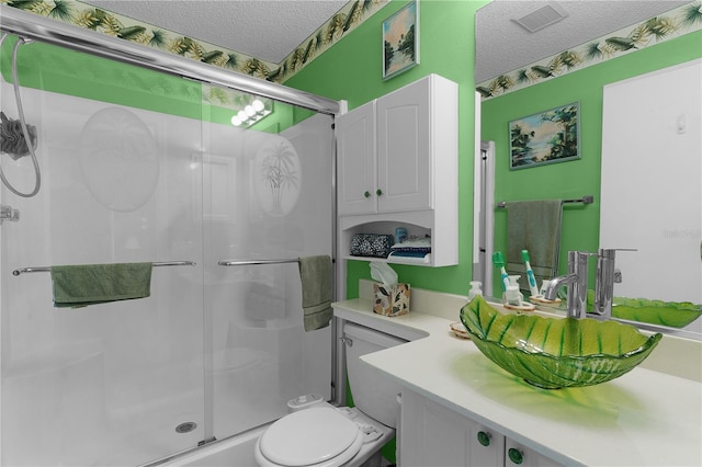 bathroom with toilet, vanity, a textured ceiling, and a shower with shower door