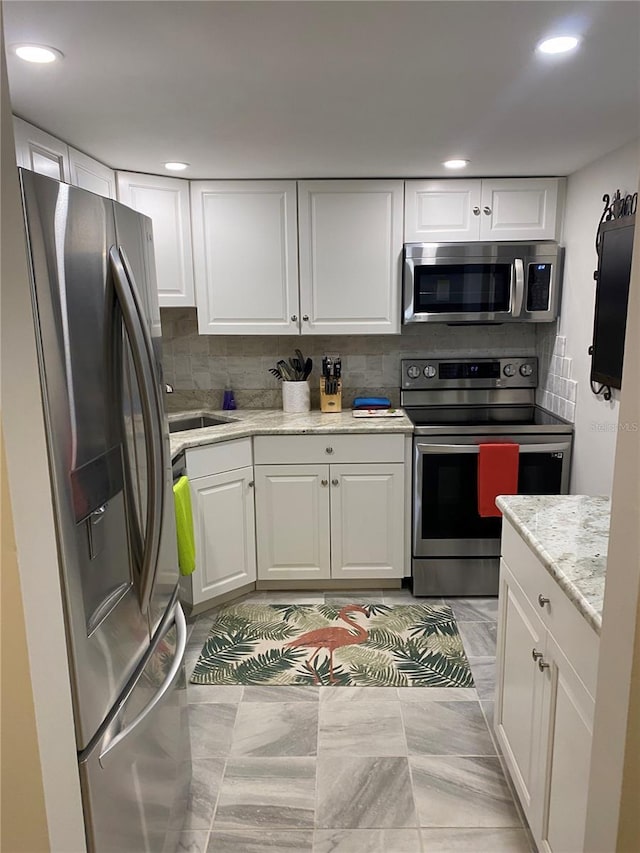 kitchen featuring appliances with stainless steel finishes, backsplash, white cabinetry, and light stone counters