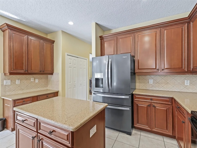 kitchen featuring light stone counters, stainless steel refrigerator with ice dispenser, backsplash, a textured ceiling, and light tile patterned floors