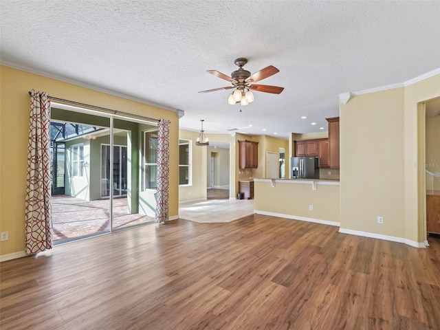 unfurnished living room with ceiling fan with notable chandelier, a textured ceiling, light wood-type flooring, and crown molding