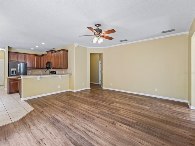 kitchen featuring crown molding, light wood-type flooring, a textured ceiling, a kitchen bar, and stainless steel fridge with ice dispenser