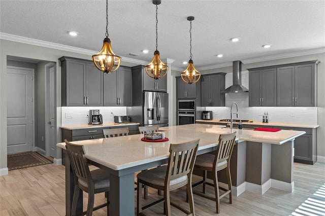 kitchen featuring decorative backsplash, appliances with stainless steel finishes, wall chimney exhaust hood, a textured ceiling, and a center island with sink