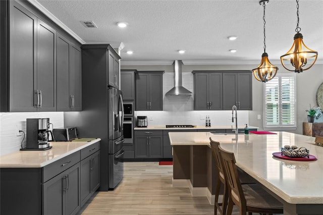 kitchen featuring light wood-type flooring, ornamental molding, wall chimney exhaust hood, sink, and pendant lighting