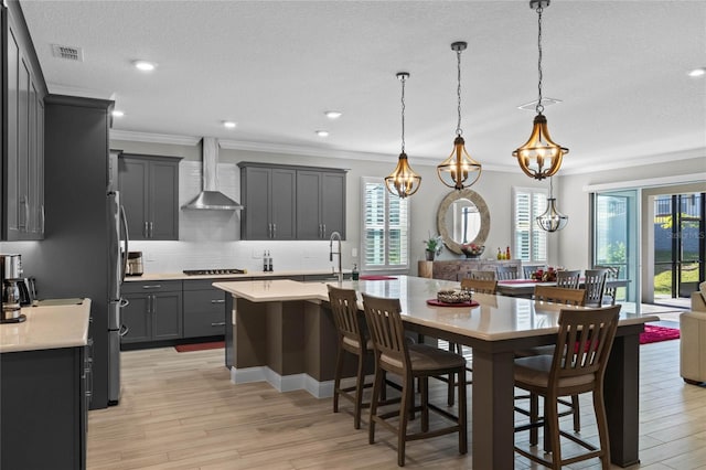 kitchen with decorative light fixtures, light hardwood / wood-style flooring, plenty of natural light, and wall chimney exhaust hood