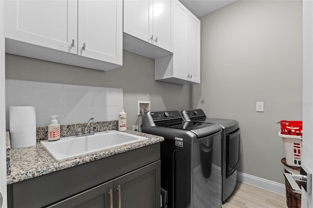 washroom with separate washer and dryer, sink, cabinets, and light wood-type flooring