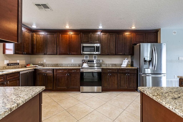 kitchen with light stone countertops, a textured ceiling, light tile patterned floors, dark brown cabinets, and stainless steel appliances