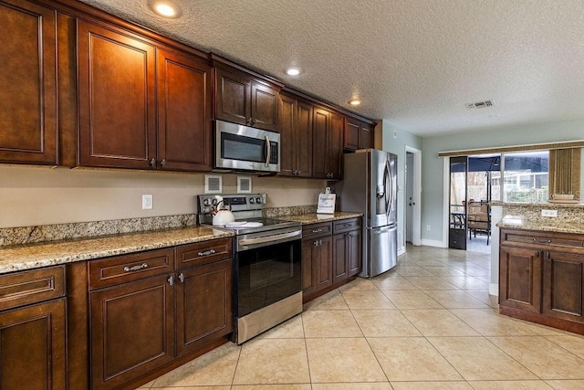 kitchen featuring light stone counters, light tile patterned floors, stainless steel appliances, and a textured ceiling