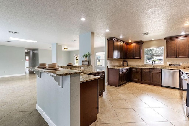 kitchen with dishwasher, a kitchen bar, stone counters, and light tile patterned flooring