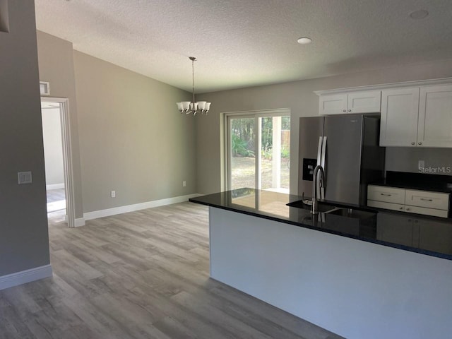 kitchen featuring stainless steel fridge, a textured ceiling, decorative light fixtures, light hardwood / wood-style flooring, and white cabinetry