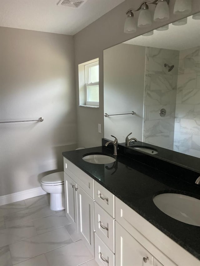 bathroom with a tile shower, vanity, and toilet