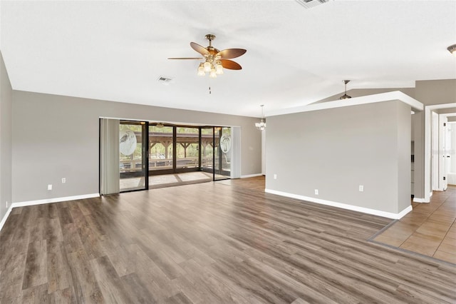 unfurnished living room with ceiling fan with notable chandelier, dark wood-type flooring, and lofted ceiling