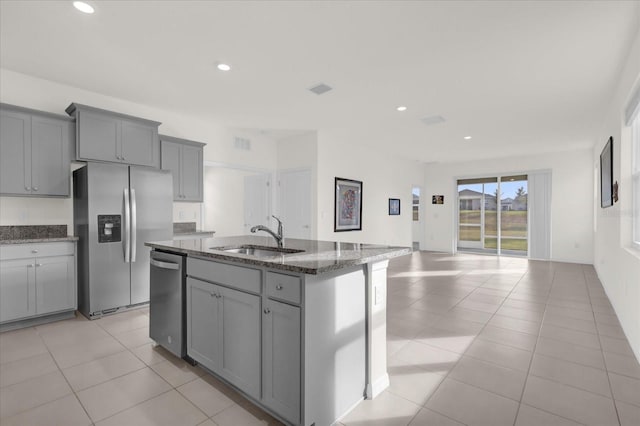 kitchen with appliances with stainless steel finishes, dark stone counters, gray cabinetry, a kitchen island with sink, and sink