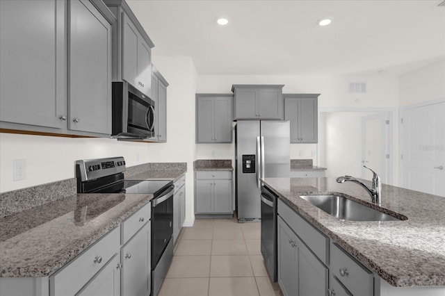 kitchen with appliances with stainless steel finishes, gray cabinetry, sink, light tile patterned floors, and a center island with sink