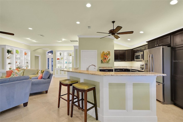 kitchen featuring a kitchen bar, ornamental molding, dark brown cabinets, stainless steel appliances, and a center island with sink