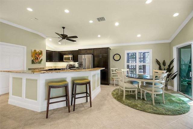 kitchen with a center island with sink, ceiling fan, ornamental molding, appliances with stainless steel finishes, and a kitchen bar