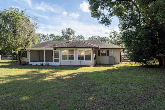 rear view of property featuring a sunroom, stucco siding, fence, and a lawn